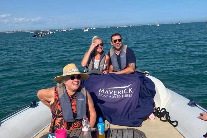 People sitting and smiling on a boat with Maverick Boat Adventures banner and clear blue sky.