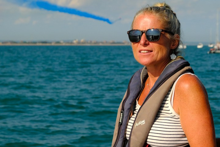 Person in sunglasses and life jacket on a boat with blue smoke trail in the sky.