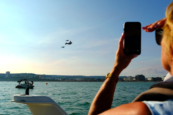 Person photographing planes flying over water and boats, sunny day.