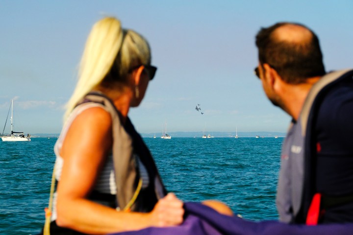 Two people on a boat watching planes flying over the sea.