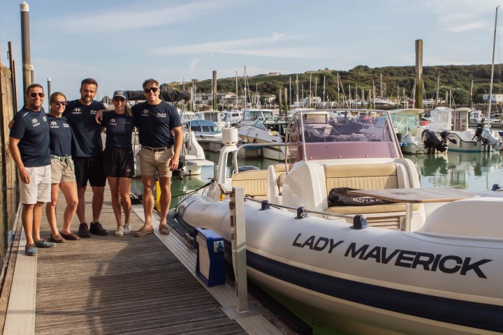 Five people standing beside a boat labeled 'Lady Maverick' at a marina on a sunny day.