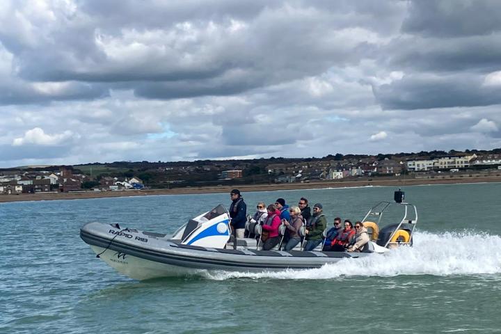 A group of people in a speedboat on the water under a cloudy sky.