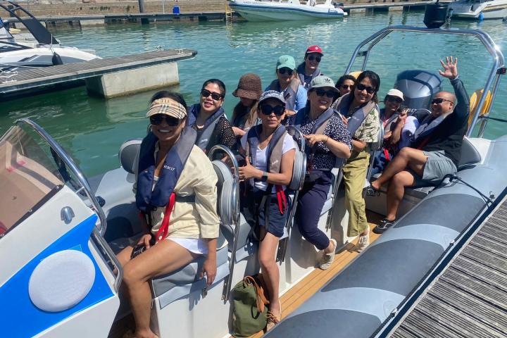 Group of people on a boat at a marina, smiling and wearing life jackets under sunny skies.