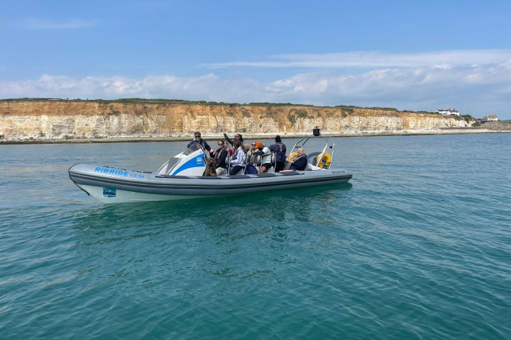 People on a speedboat in calm sea with rocky cliffs in the background on a sunny day.