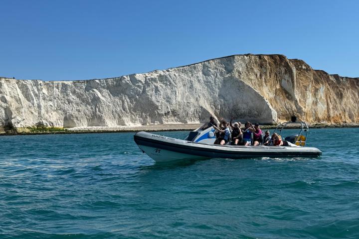 Small boat with passengers near white cliffs under clear blue sky.