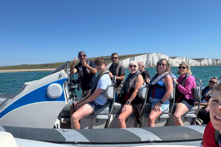 Group on a boat wearing life jackets near white cliffs under clear blue sky.