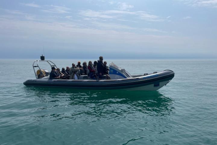 A group of people sitting on a small motorboat floating on calm water under a cloudy sky.