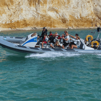 Group of people on a speeding inflatable boat near rocky cliff.