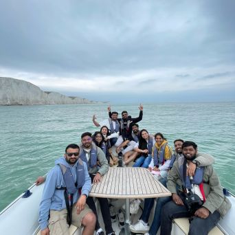 Group of people on a boat near white cliffs and calm sea, cloudy sky above.