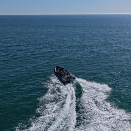 Aerial view of a speedboat gliding on open sea creating white wake behind.