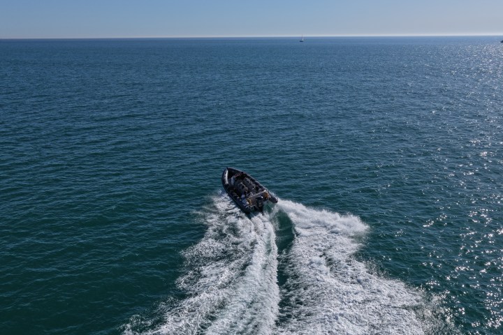 Aerial view of a speedboat gliding on open sea creating white wake behind.